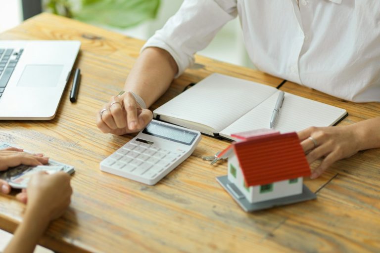 Mietverwaltung Hände eines Beraters mit Taschenrechner und Hausmodell auf einem Tisch.